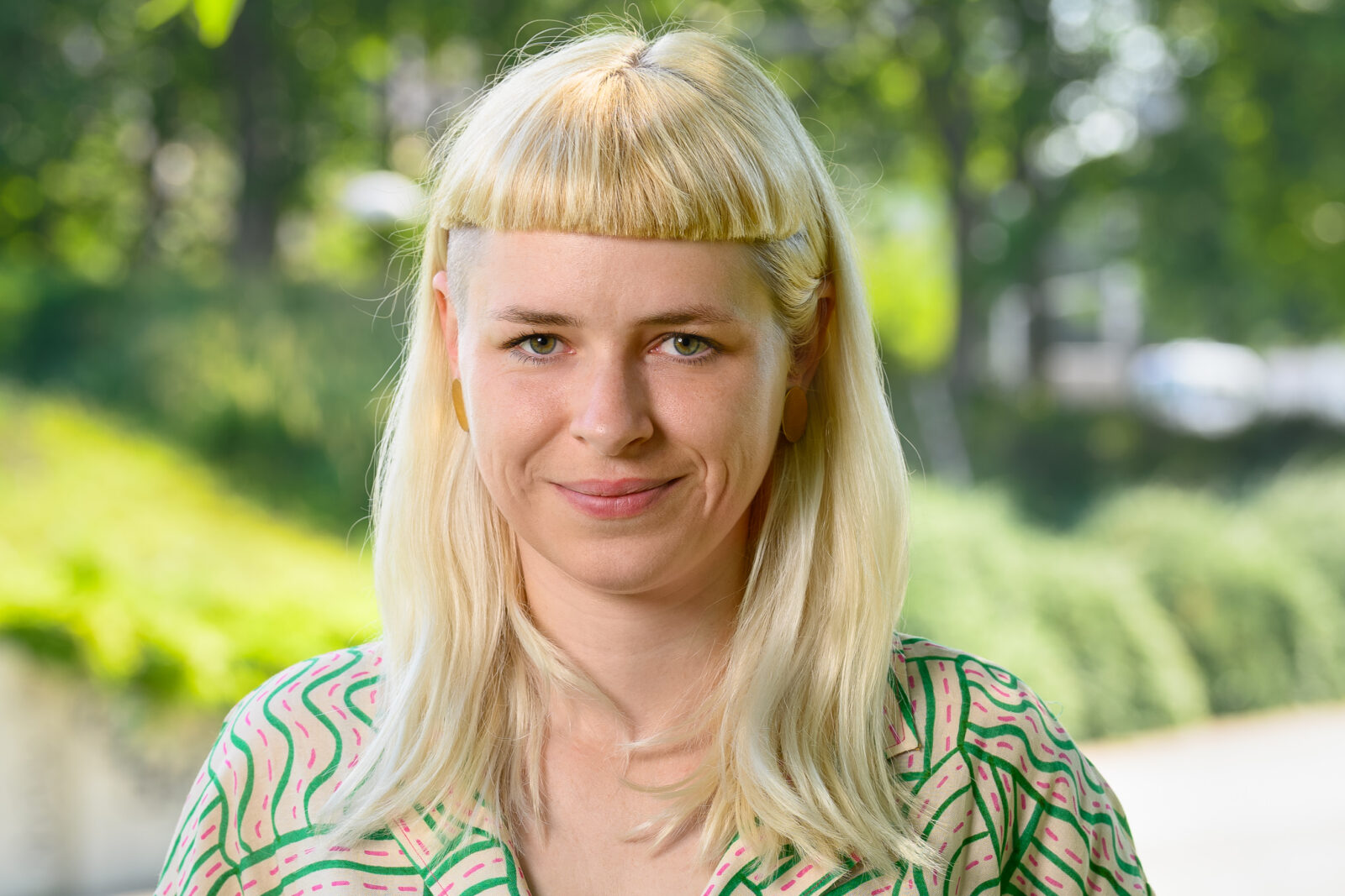 Portrait einer jungen blonden Frau mit einem grünen Hintergrund.