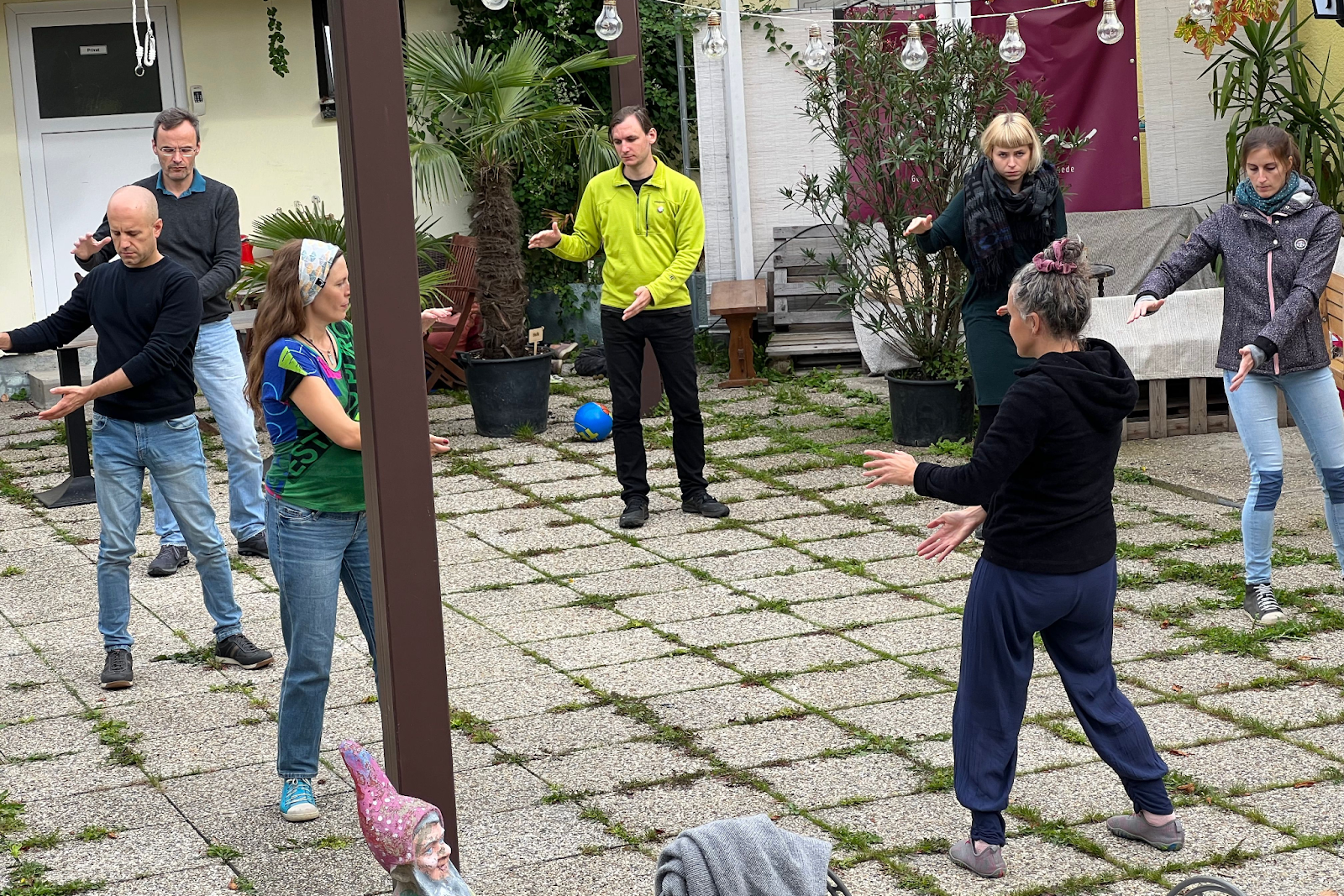 Menschen in einem Hinterhof die an einer Performance teilnehmen und eine Bewegungsübung gemeinsam ausüben bei der sie die Arme nach rechts bewegen müssen.