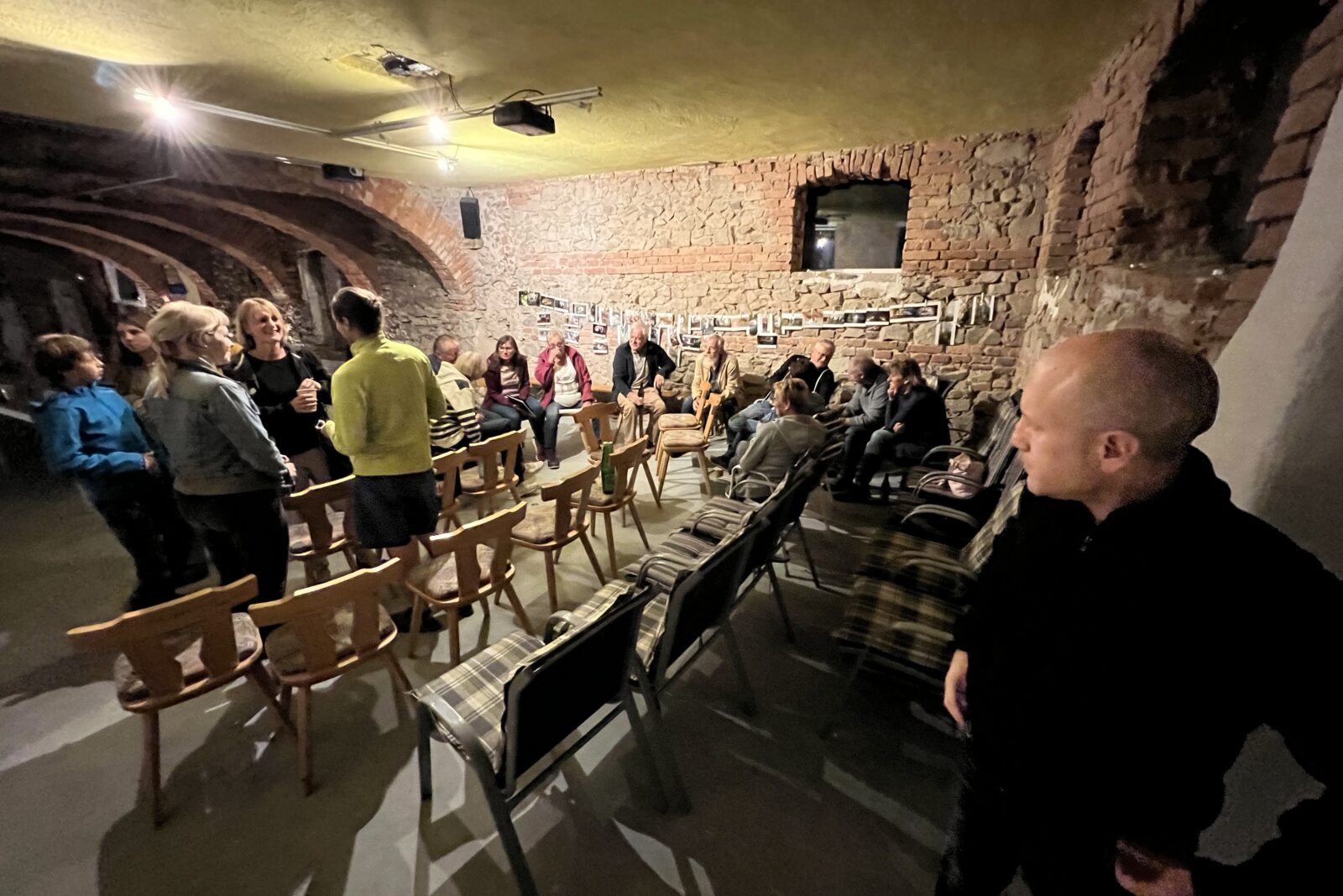Circa 15 Menschen die sich in einem Veranstaltungsraum miteinander unterhalten der mit Stühlen ausgestattet ist.